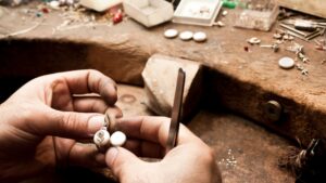 image of a local jeweler working on a customers jewelry at the work bench with various jewelry pieces on a wooden table in the background