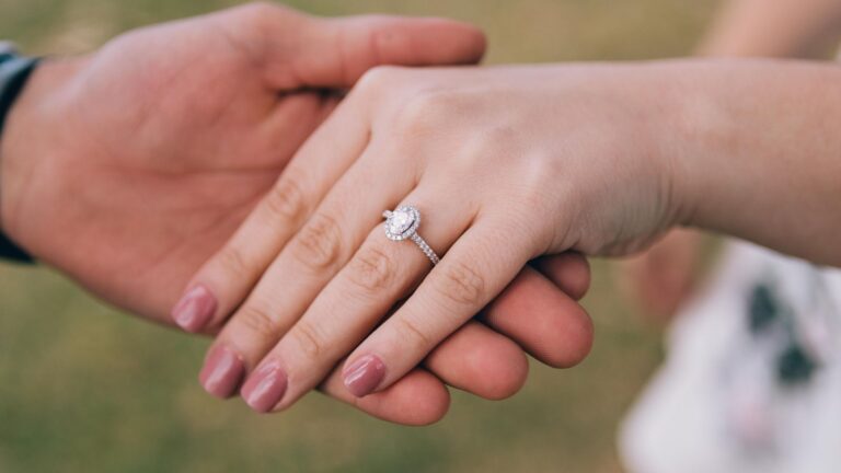 an image of a women's hand being held by a man with a white gold diamond engagement ring on her finger to signify marriage