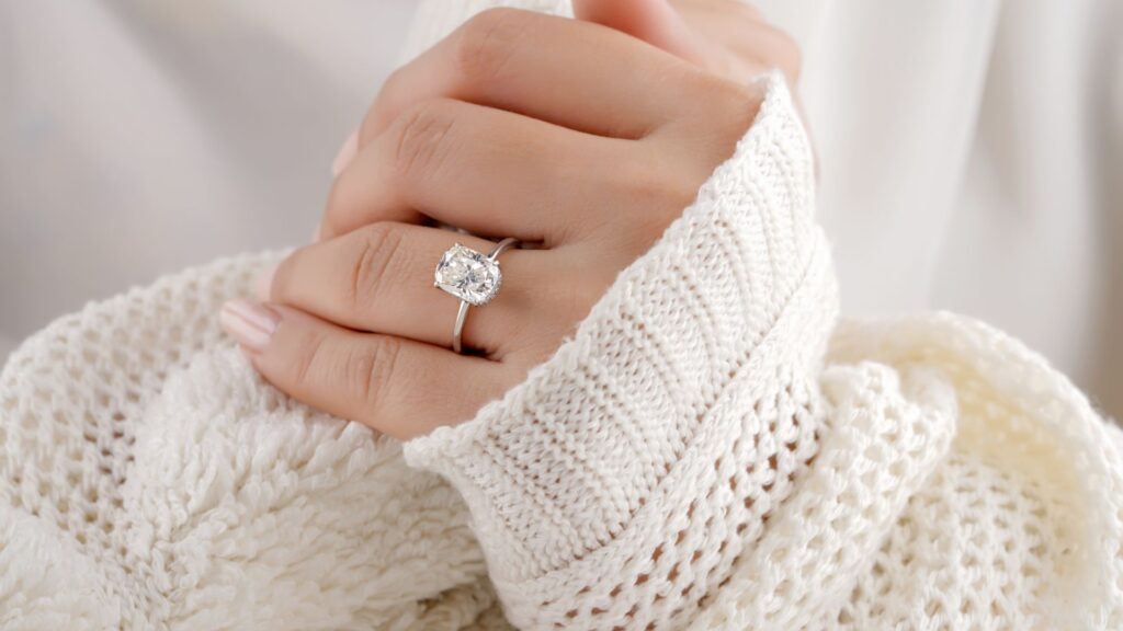 an image of a womens hands in a longsleeve sweater displaying an engagement ring on her finger